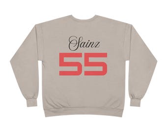 May include: A light tan sweatshirt with the name "Sainz" in black script above the number "55" in red block letters. The sweatshirt has long sleeves and a crew neck.