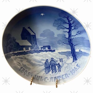 May include: A blue and white decorative plate featuring a winter scene with a church, a tree, and figures walking in the snow. The plate has the text "1895 JULC AFTER 1965" around the edge.
