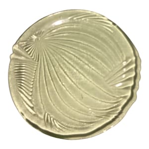 May include: A clear, circular glass plate with a decorative, fan-like pattern. The plate has a scalloped edge and a central design radiating outwards. The glass has a slight yellow tint, and the design is embossed into the surface.