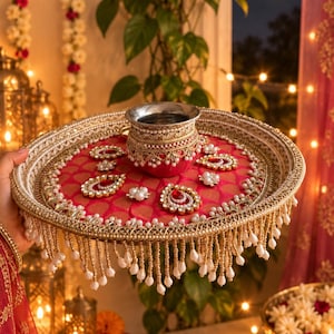 May include: A round decorative tray featuring a vibrant pink fabric center with a repeating pattern, adorned with gold metallic trim, faux pearls, and teardrop-shaped embellishments. A matching small metal pot sits in the center of the tray.
