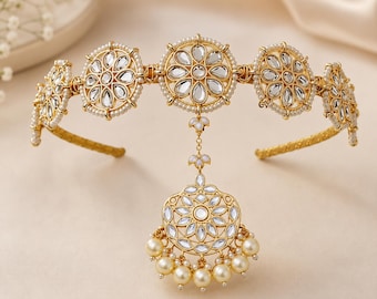 May include: A gold-toned metal headband featuring five circular floral motifs set with clear, teardrop-shaped stones and bordered by small white pearls. A central dangling pendant with matching stones and a row of hanging cream-colored pearls.