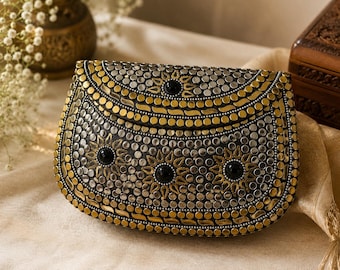 May include: A black clutch bag featuring a curved flap and a structured body, heavily embellished with a dense pattern of circular gold and silver metallic studs, interspersed with small black circular cabochons arranged in floral-like motifs.