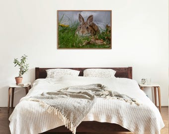 May include: A framed print of a brown rabbit resting in green grass. The rabbit has long ears and is surrounded by foliage. The artwork is displayed above a bed with white bedding and a decorative throw blanket.