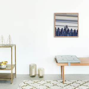 May include: A framed photograph featuring a squirrel perched atop a dark blue wooden fence. The photograph is in a light brown wooden frame. The background shows a white and gray building.