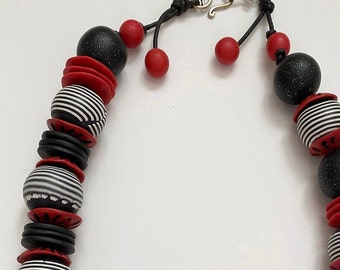 Polymer bead necklace of carved red beads and layered black and white beads; with hand forged silver metal clasp.