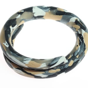 May include: A thick, twisted bangle bracelet with a camouflage pattern in shades of black, white, beige, and silver.