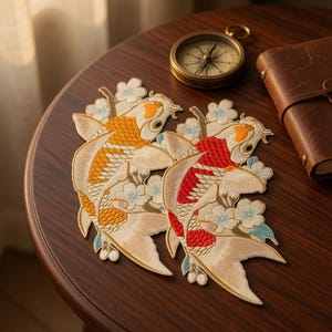 May include: Two embroidered koi fish patches featuring intricate scale detailing in vibrant orange and red hues, accented with light blue and white cherry blossom motifs. The patches are displayed with a compass and a leather-bound notebook.