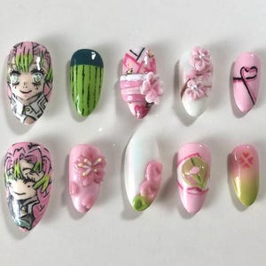 May include: A set of ten artificial nails with various designs. The designs include anime character art, watermelon, floral accents, and abstract patterns. Colors include pink, green, white, and black. The nails are oval-shaped and appear to be professionally done.
