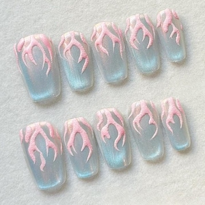 Puede incluir: Juego de diez uñas postizas con base transparente y brillo iridiscente azul-verdoso. Cada uña presenta un diseño de llama rosa, creando un look único y elegante. Las uñas son de forma rectangular.