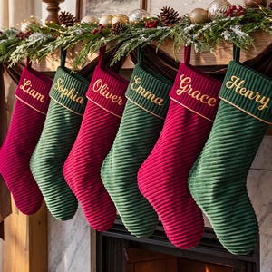 Peut inclure: Six chaussettes de Noël en velours côtelé alternant les couleurs rouge profond et vert forêt. Chaque chaussette présente un revers avec des noms brodés en fil doré : Liam, Sophia, Oliver, Emma, Grace et Henry.