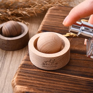 May include: Two wooden aromatherapy diffusers with a ball-shaped insert. One is light-colored, the other is dark. The light-colored diffuser has a mountain and tree design with the text "Robert & Emily".