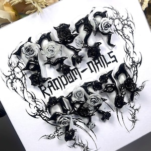 Puede incluir: Un conjunto de uñas postizas con un diseño gótico. Las uñas son transparentes con detalles de rosas negras y grises y adornos negros. El texto "RANDOM-NAILS" está impreso sobre un fondo blanco.