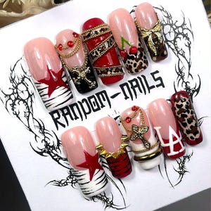 May include: A set of ten artificial nails with various designs. The nails feature a range of colors, including pink, red, black, and gold. Some nails have star, cherry, and leopard print designs, while others have gold chain and cross accents. The text "RANDOM-NAILS" is visible.