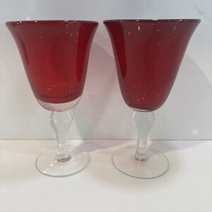 May include: Two red wine glasses with clear stems and bases. The glasses have a tulip-shaped bowl and a clear, bulbous stem. The bases are round and flat. The glasses are made of glass and are likely hand-blown.