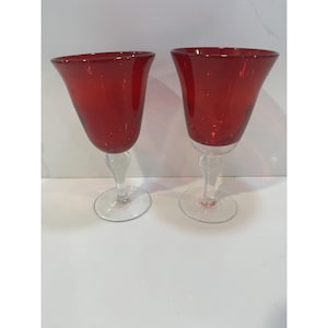 May include: Two red wine glasses with clear stems and bases. The glasses have a flared bowl shape and a vibrant red color. The stems are elegantly curved, and the bases are circular.