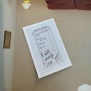May include: A guest check with handwritten notes and the words "I will always love you" in red ink. The check is on a beige wall, with a partial view of a light fixture and a brown sofa.