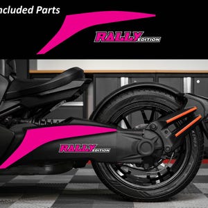 May include: A black Can-Am Ryker with hot pink "Rally Edition" decals. The decals are on the side panel and include the text "Rally Edition". The image also shows the rear tire and suspension.