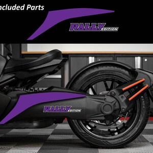 May include: Purple "Rally Edition" decals for a motorcycle. The decals are shown on the side of the vehicle, with the text in white and purple. The image also shows the rear wheel and other parts of the motorcycle.