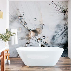 May include: A modern bathroom featuring a white, freestanding bathtub. The wall behind the tub showcases a large-scale, artistic mural of a dandelion seed head with water droplets. The room has a wooden floor and a minimalist design.