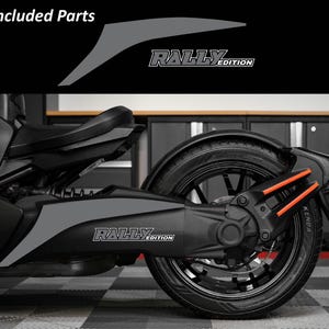 May include: A black and gray motorcycle with the text "Rally Edition" on the side. The image shows the rear wheel and suspension components, with orange accents. The words "Included Parts" are at the top.