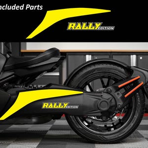 May include: Black and yellow motorcycle decals with the text "RALLY EDITION". The decals are yellow with black accents and are designed to fit on the side of a motorcycle. The image also shows the rear wheel and suspension.