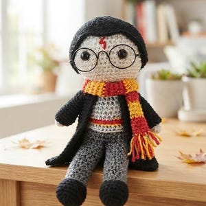 May include: A handcrafted crochet doll featuring a character with black hair, round black glasses, and a red lightning bolt mark on the forehead. The doll wears a black coat, a grey jumper, grey trousers, black shoes, and a red and yellow striped scarf.