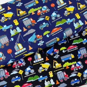 May include: Two fabric swatches with a construction vehicle pattern. One swatch is navy blue, the other black. The pattern includes trucks, excavators, cranes, traffic lights, and road signs. The signs read "STOP" and "SLOW".