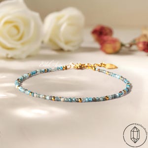 Può includere: Delicato braccialetto di perline con piccole perle azzurre e dorate. Il braccialetto ha una chiusura dorata ed è esposto su una superficie bianca. Il logo EdelAuraStudio è in basso a destra.