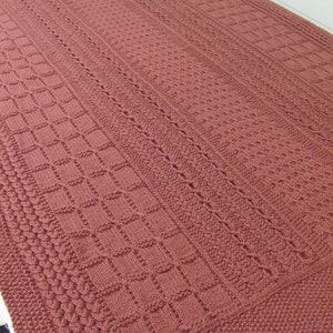 May include: A knitted throw blanket in a deep burgundy color with a variety of woven patterns.