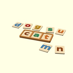 May include: A wooden educational toy set featuring square tiles with colorful letters. The tiles spell out the words dog, cat, sun, and mn. A rectangular wooden tray with three slots holds the letters c, a, and t in a horizontal row.