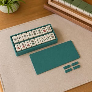 May include: A set of off-white Mahjong tiles with black, red, and green characters and symbols, arranged in a teal rectangular tray. A matching teal rectangular cover is placed beside the tray, along with four small, separate teal rectangular pieces.