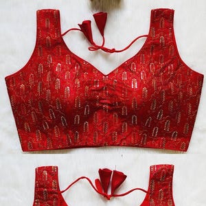 May include: Red sleeveless blouse with gold-colored embroidered floral pattern. The blouse has a V-neckline and a tie detail at the back. The fabric appears to be silk. The text "kashmiri-silk-thread-work-blouse-301" is visible.