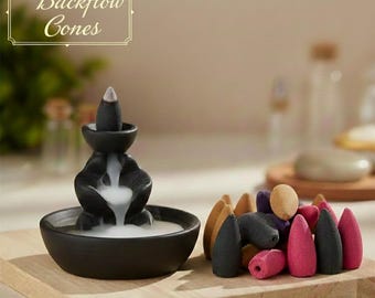 Peut inclure: Un brûleur d'encens à refoulement en céramique noire avec un effet de fumée en cascade. Le brûleur est accompagné d'une variété de cônes d'encens colorés dans les tons de marron, violet, noir et rose. Le texte "Backflow Cones" est en haut à gauche.