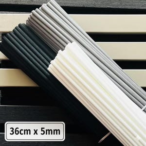 Peut inclure: Ensemble de fines baguettes striées noires, grises et blanches. Les baguettes sont regroupées, avec les dimensions de 36 cm x 5 mm affichées sur un rectangle blanc. Le fond présente des rayures horizontales noires et crème.