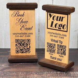 May include: Two wooden table signs with dark brown accents. One sign reads "Book Your Event" and the other says "Your Logo". Both signs include a website, phone number, and QR code. One sign also says "Virtual Tip".