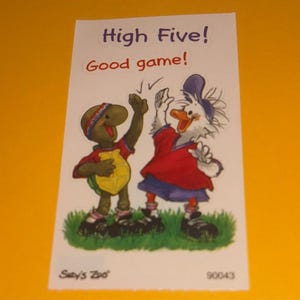 May include: A rectangular card with a cartoon illustration of a turtle and a duck giving each other a high five. The text "High Five! Good game!" is written at the top. The card is on a yellow background.