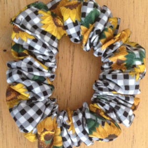 May include: A black and white checkered fabric hair scrunchie with a sunflower print. The scrunchie is made of soft, stretchy fabric and is perfect for holding hair in place.