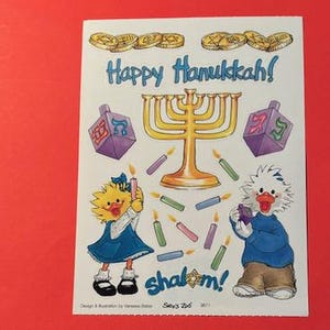 May include: A sticker sheet with a menorah, dreidels, and two cartoon characters. The text on the sticker sheet says "Happy Hanukkah!" and "Shalom!"