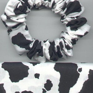 May include: A black and white cow print scrunchie hair tie. The scrunchie is made of soft fabric and is perfect for holding back hair.