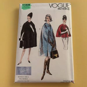 May include: A Vogue Patterns sewing pattern envelope, V1838, featuring illustrations of three capes. The white envelope displays text including Vogue Patterns, Reissue Circa 1963 Design, and size information. The illustrations show capes in black, blue, and red.