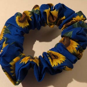 May include: A blue scrunchie with a sunflower pattern. The scrunchie is made of fabric and has a gathered look.