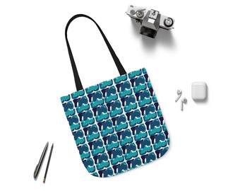 Puede incluir: Un bolso tote blanco con un patrón repetido de formas abstractas azules y turquesas. El bolso tiene asas negras. Una cámara vintage, bolígrafos y auriculares inalámbricos también están sobre la superficie blanca.