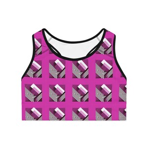 Op de afbeelding: Een magenta sportbeha met een herhalend geometrisch patroon. Het patroon bevat witte, zwarte en paarse rechthoekige vormen met gestreepte en effen elementen. De beha heeft een zwarte rand en bandjes.