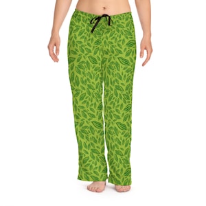 Puede incluir: Pantalones de pijama verdes con un estampado de hojas. Los pantalones tienen una cintura con cordón y un diseño repetido de hojas verdes sobre un fondo verde claro. Los pantalones de pijama están hechos de un material suave y cómodo.