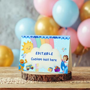 May include: A light blue party invitation with a rainbow, sun, and cartoon characters. The invitation is on a wooden base, with pink, blue, and gold balloons in the background. The text on the invitation reads "EDITABLE Custom text here."