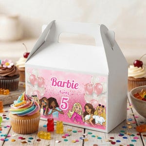 May include: A white party favor box with a handle, decorated with a pink background and the text "Barbie turns 5." The box features illustrations of Barbie and pink balloons. Cupcakes and gummy candies are in the background.