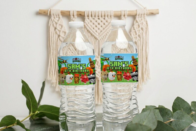 以下が含まれることがあります： 白いキャップが付いた透明なプラスチック製のウォーターボトルが2本。各ボトルには「SAM'S 8TH BIRTHAY」の文字とMinecraftをテーマにしたグラフィックが描かれたラベルが付いています。ボトルはマクラメの壁掛けの前にあります。