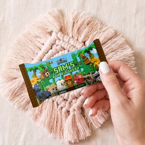以下が含まれることがあります： Minecraftをテーマにしたカラフルなキャンディーバーの包装紙が、手によって持たれています。「SAM'S 8TH BIRTHDAY」の文字と、様々なピクセル化されたキャラクターが描かれています。デザインは緑、茶色、青で、ジャングルをテーマにしています。