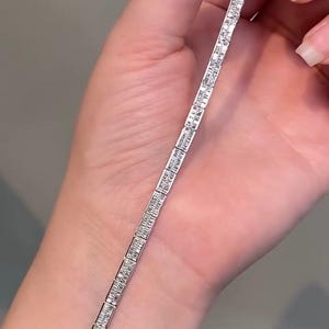 Pu&ograve; includere: Un bracciale tennis color argento caratterizzato da una fila continua di pietre trasparenti rettangolari taglio baguette incastonate in una montatura metallica. Il bracciale presenta un design lineare uniforme con ogni pietra fissata in una montatura in metallo lucido.