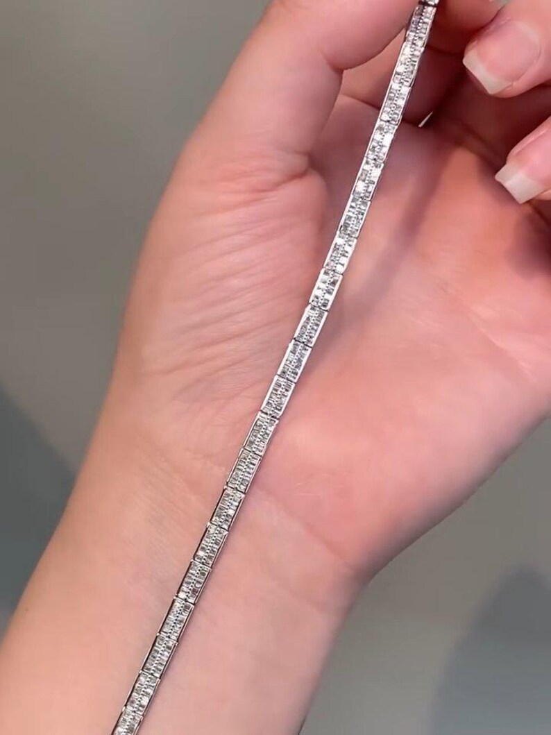 Pu&ograve; includere: Un bracciale tennis color argento caratterizzato da una fila continua di pietre trasparenti rettangolari taglio baguette incastonate in una montatura metallica. Il bracciale presenta un design lineare uniforme con ogni pietra fissata in una montatura in metallo lucido.